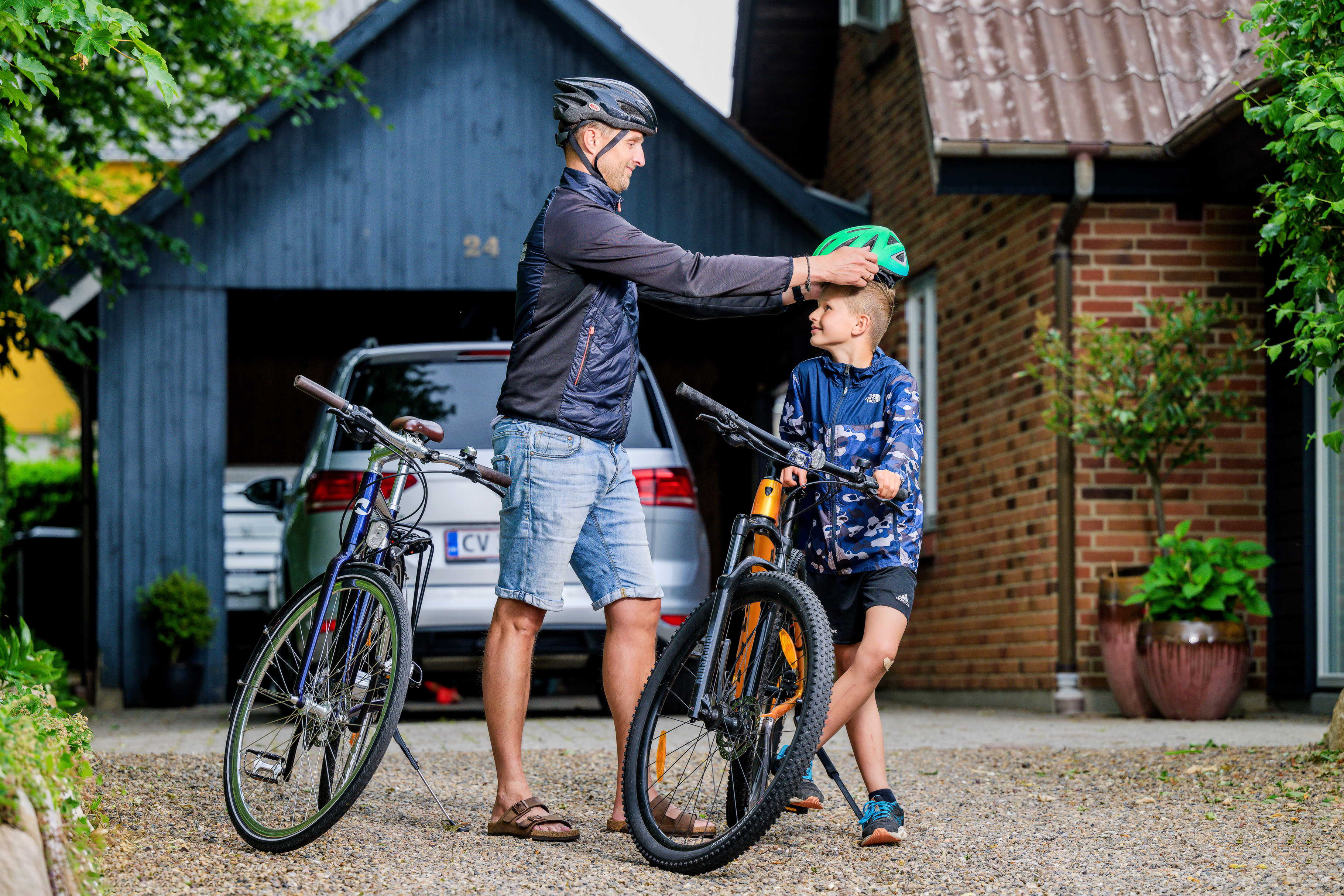 Far giver sin søn cykelhjelm på foran familiens hus og garage